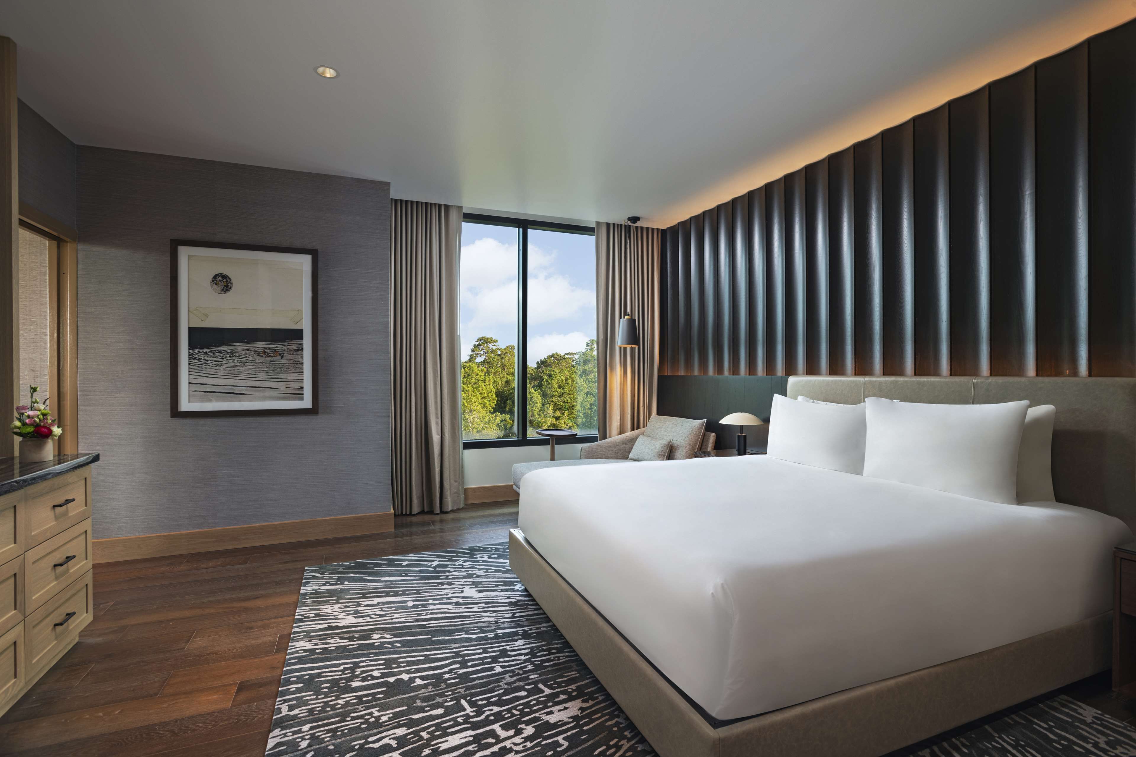 A modern hotel room with a large bed, a desk, and a view of the outdoors.