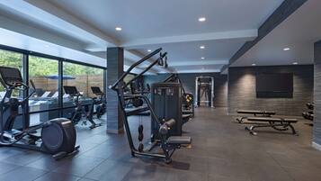 A modern gym with various exercise equipment, large windows, and a bench area.