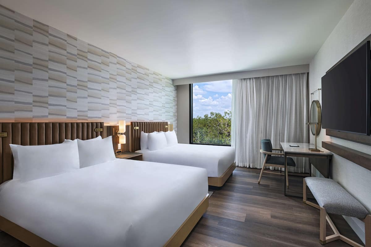 A hotel room with two beds, a desk, a chair, a TV, and a window with curtains.