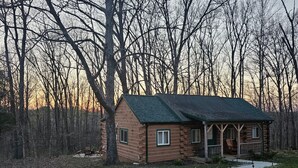 A log cabin with a green roof, surrounded by trees, and a gravel path leading to it. - Perfect Cabin for Fisherman and Families (French Lick)