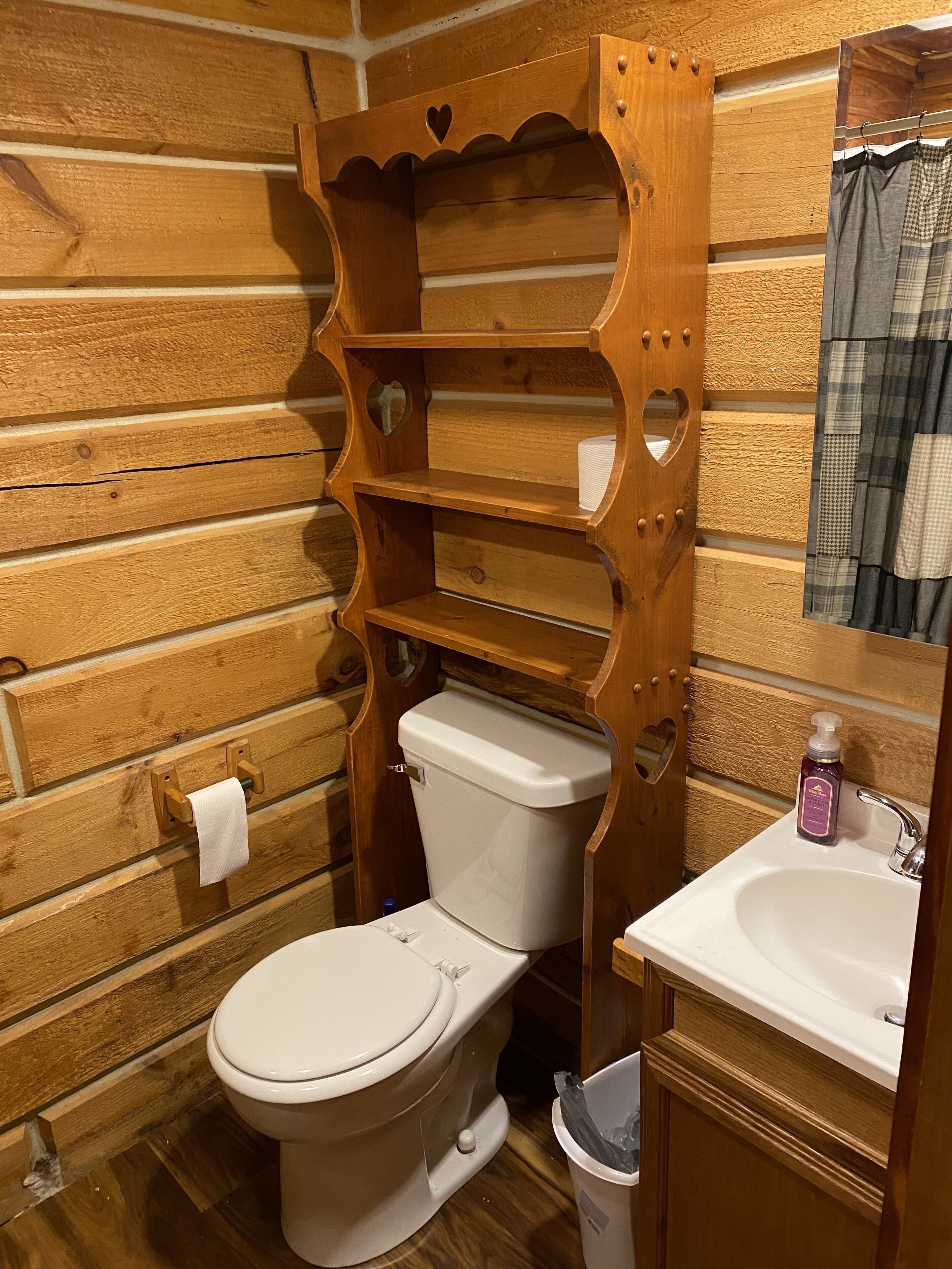 A wooden bathroom with a toilet, a sink, and a shelf unit with heart-shaped cutouts.