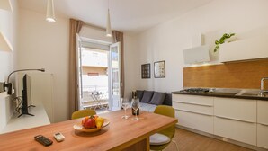 Een knus keuken met een eethoek, een kleine tafel met fruit en wijnglazen, een bank en uitzicht door een open deur.