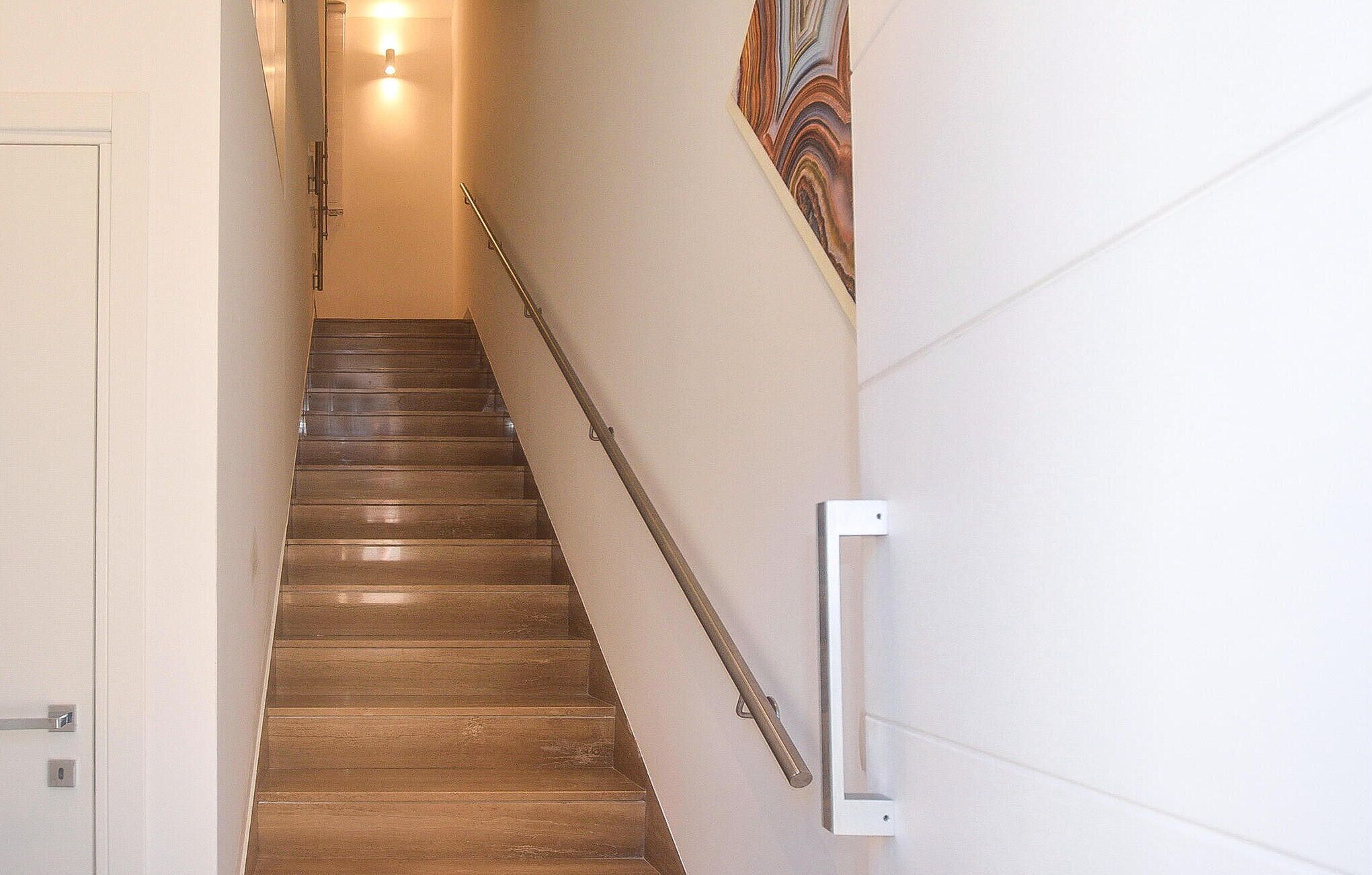 Escada de madeira com corrimão, luminária no topo e interruptor de luz fixado na parede.