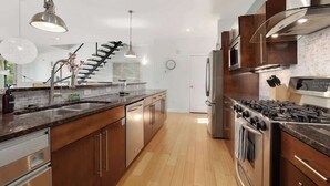 Una cocina moderna con una isla central, electrodomésticos de acero inoxidable y una escalera que sube a otro nivel.