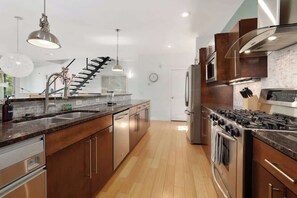A modern kitchen with a central island, stainless steel appliances, and a staircase leading to another level. - Noble Nest - 5 Min to Downtown and U of A (Fayetteville)