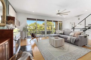 A spacious living room with a grey sofa, a coffee table, and a large window offering a view of trees. - Noble Nest - 5 Min to Downtown and U of A (Fayetteville)