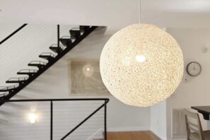 Un intérieur moderne avec un escalier, un luminaire suspendu et une horloge au mur.