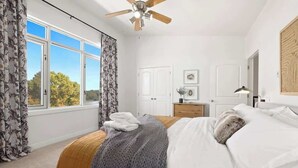 Un dormitorio con cama, ventilador de techo, ventana con cortinas, cómoda y puerta.