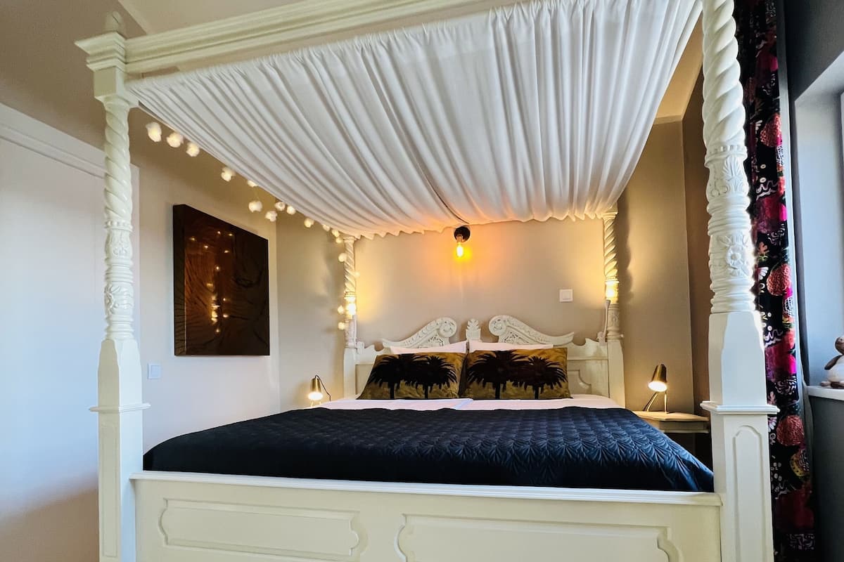 A four-poster bed with a canopy, a dark blue bedspread, and two decorative pillows.