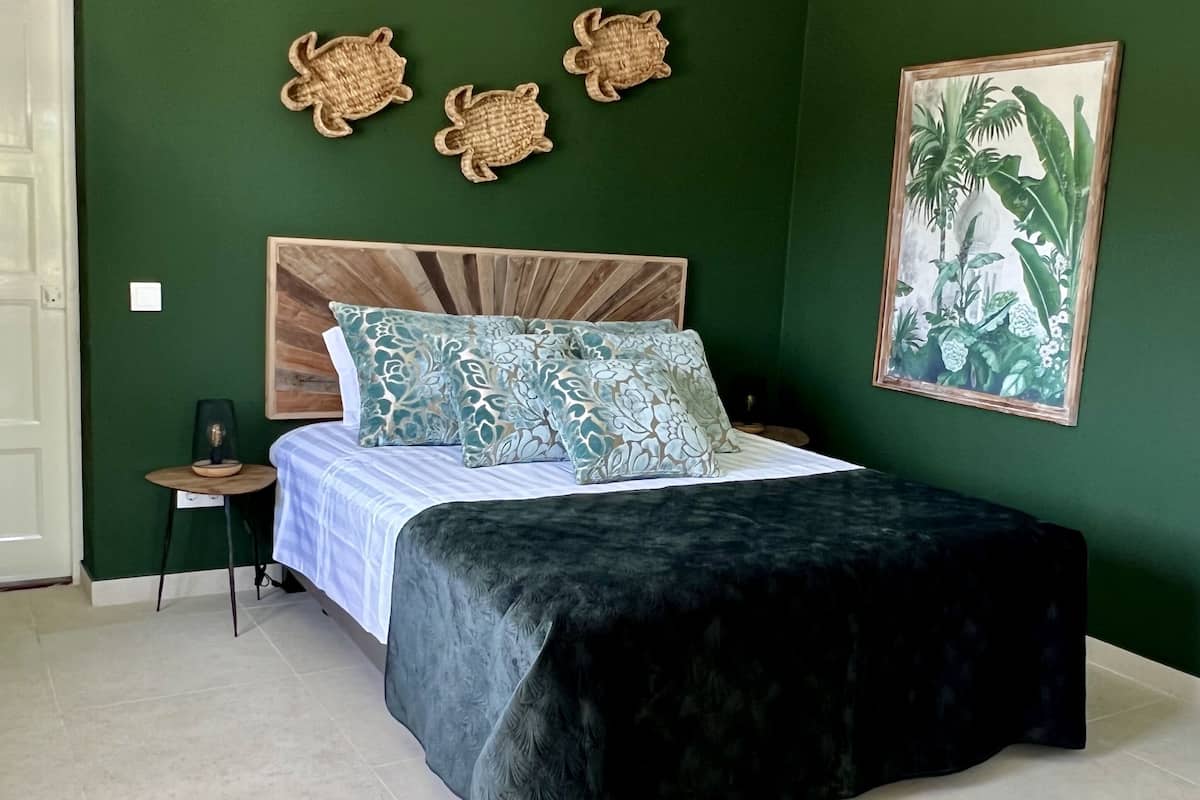 A bedroom with a bed, a nightstand, a wall-mounted turtle decoration, and a framed plant painting.