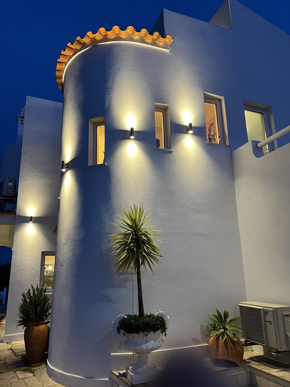 A building with a curved facade, multiple windows with lights, and potted plants. - Palm View Guesthouse-Adults only (Lagos)