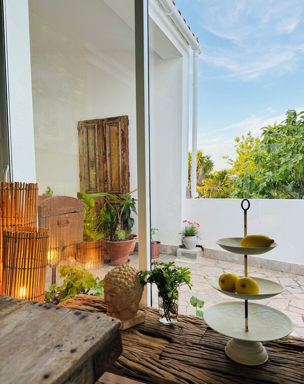 Un espace patio aménagé avec une table en bois, des plantes en pot et un présentoir à plusieurs niveaux où sont disposés des citrons.