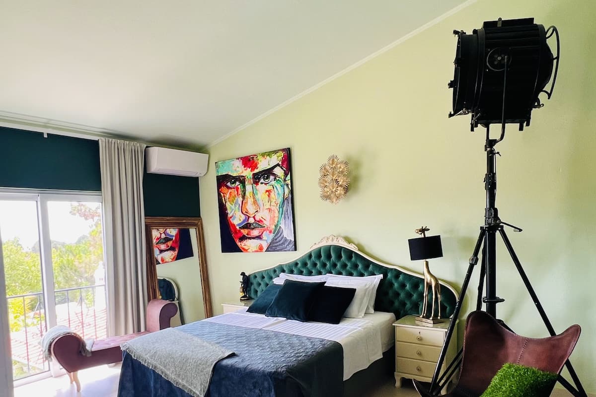 A bedroom with a bed, a chair, a tripod, and a painting.