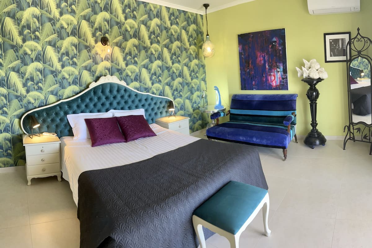 A bedroom with a bed, a nightstand, a dresser, a bench, a chair, a lamp, a painting, and a mirror.