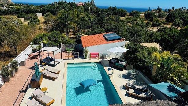 A rooftop pool area with lounge chairs and umbrellas, surrounded by lush greenery and overlooking a coastal landscape. - Palm View Guesthouse-Adults only (Lagos)