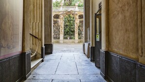 A corridor with stone flooring, columns, and a view of a garden with statues and a fountain. - Garibaldi Glamorous Apartment by Wonderful Italy (Genova)