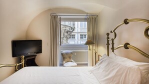 A hotel room with a bed, a television, a lamp, and a view of a building through a window with curtains. - Garibaldi Glamorous Apartment by Wonderful Italy (Genova)