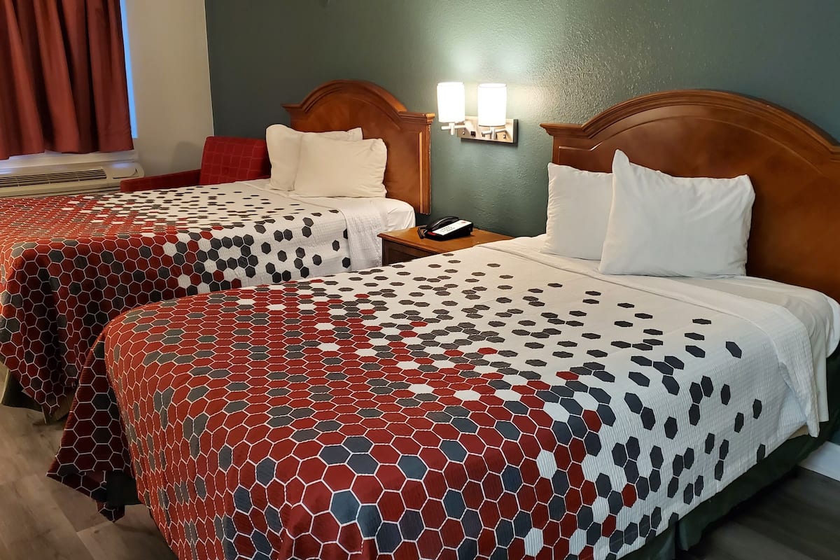 A hotel room with two beds, each with a patterned bedspread, a wooden headboard, bedside lamps, and a telephone on the nightstand.