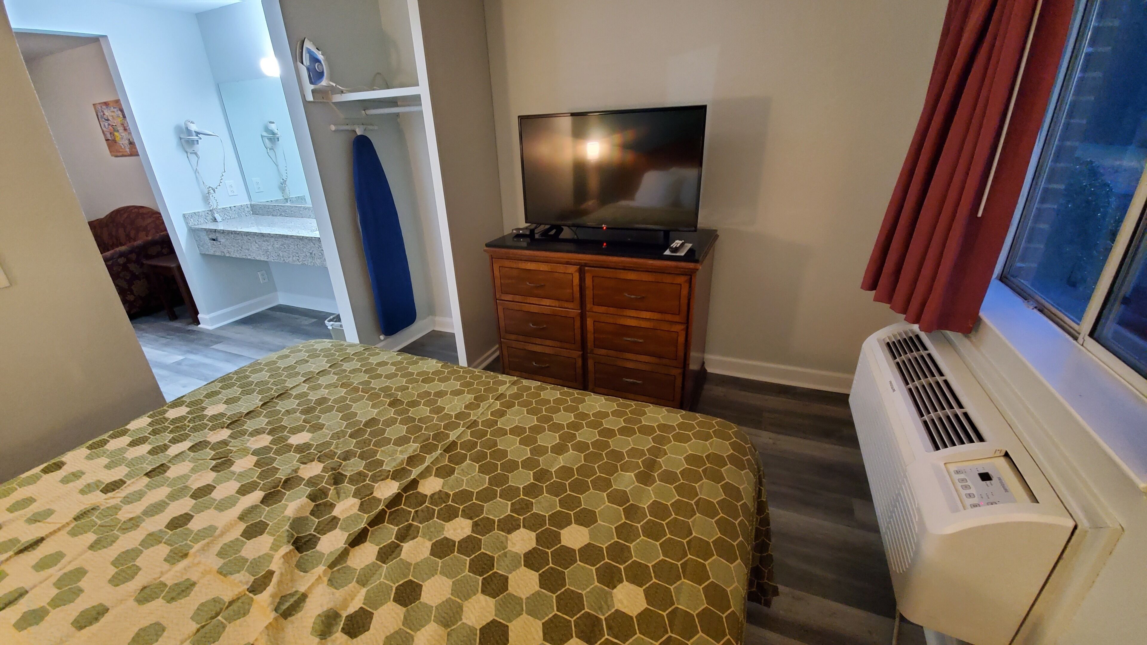 Une chambre d’hôtel avec un lit, un téléviseur posé sur une commode, un radiateur et une salle de bain visible à travers une porte ouverte.