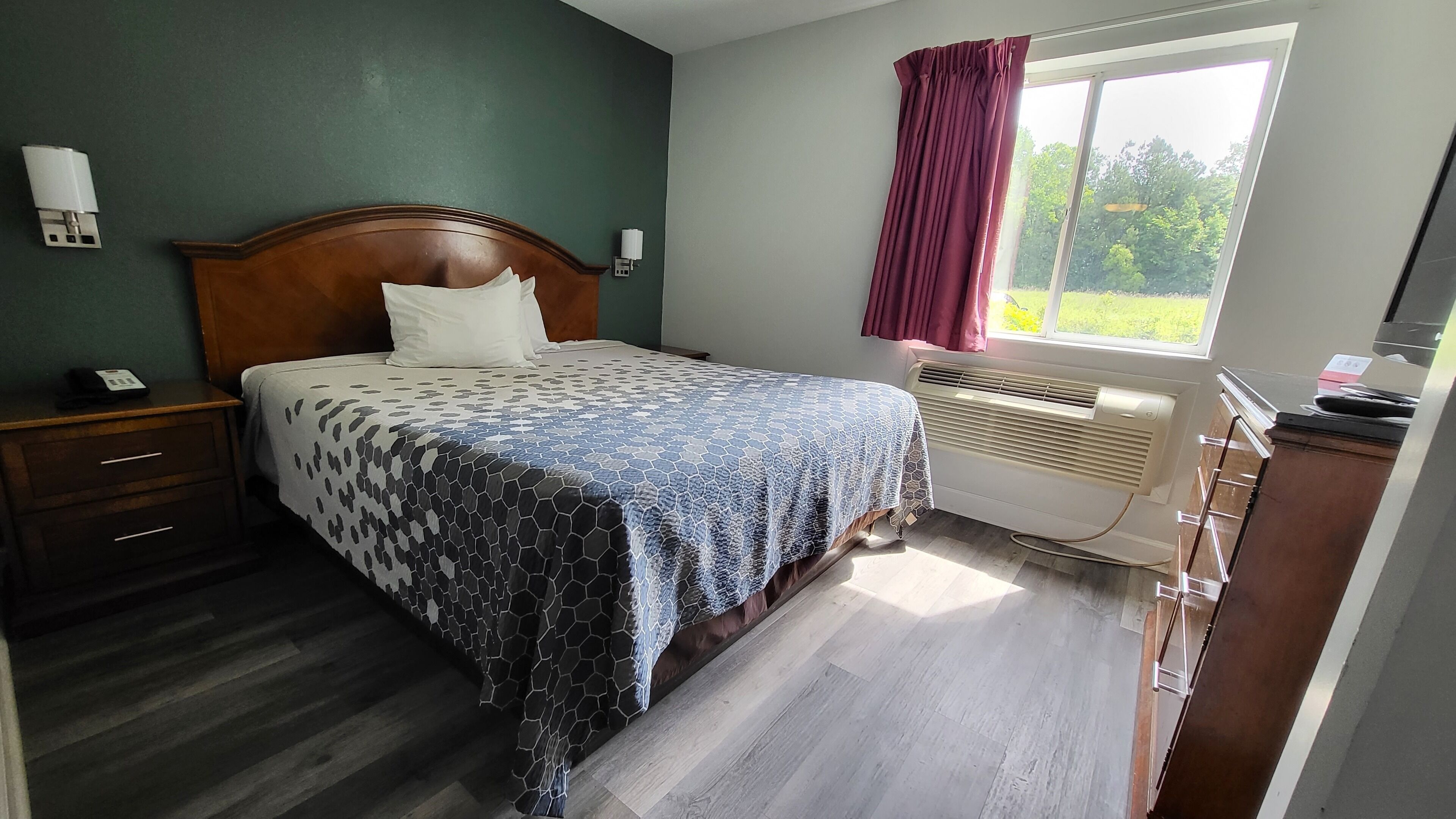 A bedroom with a bed, a nightstand, a heater, and a window with curtains.