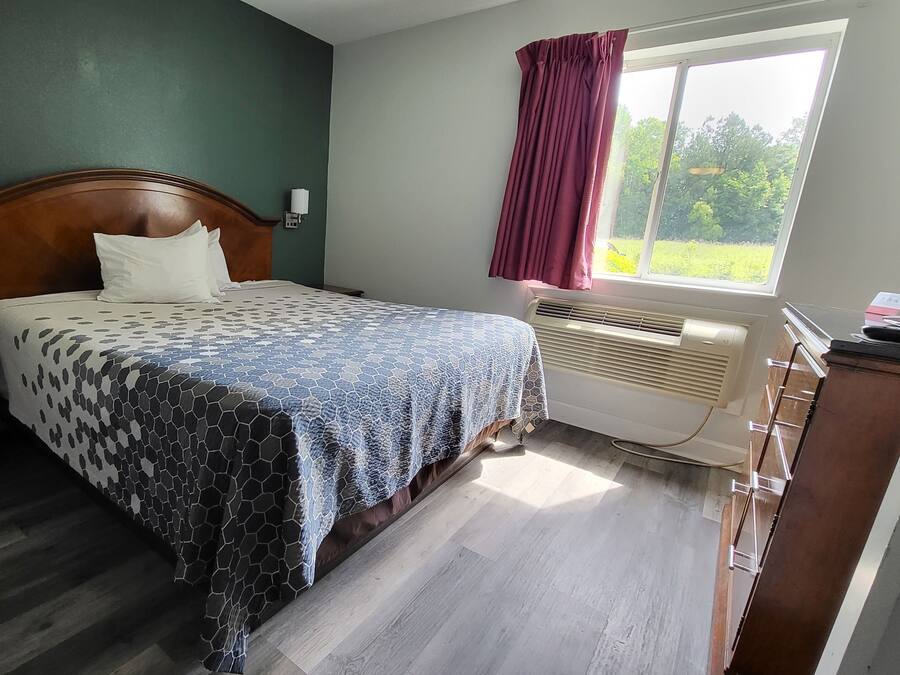 A bedroom with a bed, a nightstand, a heater, and a window with curtains.