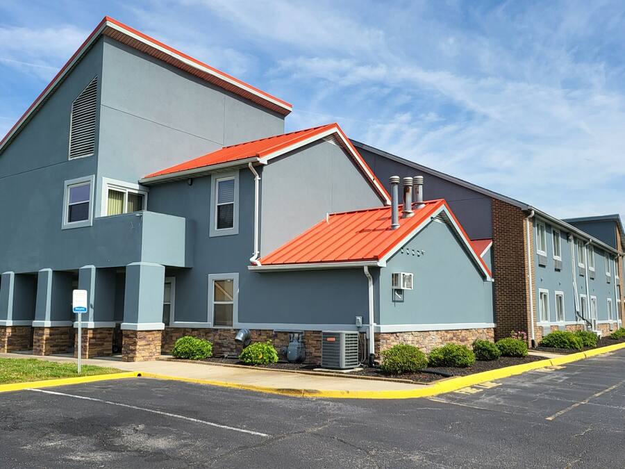 A modern building with a grey facade and red roof, featuring a guest registration area and a parking lot.