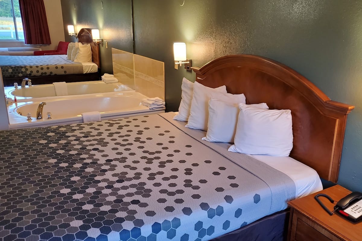 A hotel room with a large bed, a bathroom with a bathtub, and a bedside phone.