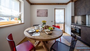 A modern kitchen with a round wooden table, chairs, and a view of the city. - CHALET INES - Appartamento 4 (Vodo Cadore)