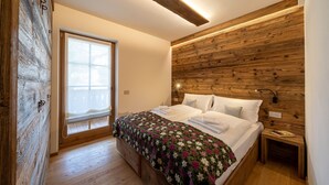 A bedroom with a wooden headboard, a large window, a bed with a floral bedspread, and a bedside table with a lamp. - CHALET INES - Appartamento 4 (Vodo Cadore)