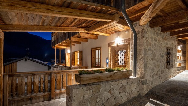 A rustic wooden staircase leading to a stone-walled balcony with wooden railings and a view of the mountains at dusk. - CHALET INES - Appartamento 4 (Vodo Cadore)