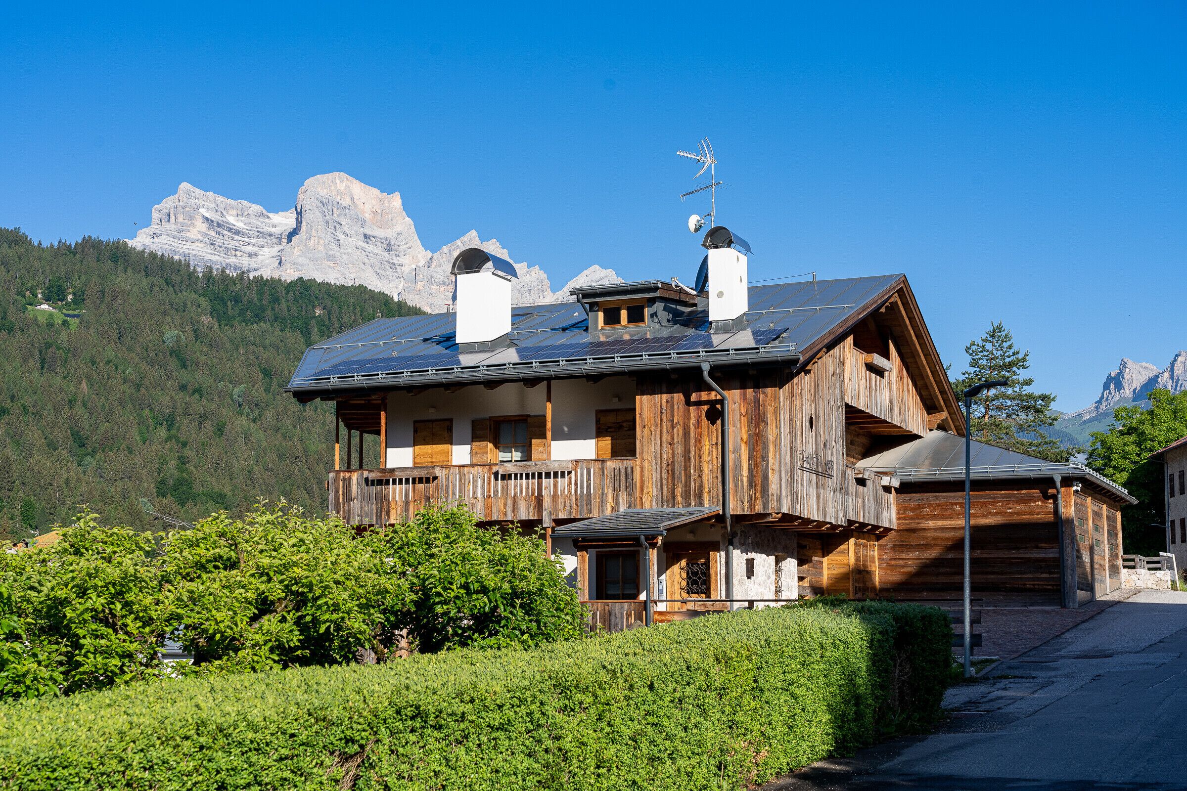 A wooden chalet with a balcony, solar panels, and a mountain backdrop.