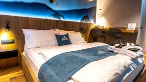 A hotel room with a bed, a wooden headboard, a wall mural, a desk with chairs, and a nightstand with a lamp. - TEVERONE SUITES & WELLNESS - Camera Gallo Forcello (Lamosano)