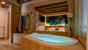 A wooden cabin interior with a large bathtub, wooden walls, a mirror, and a bed with a nightlight. - TEVERONE SUITES & WELLNESS - Camera Civetta (Lamosano)