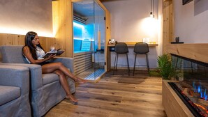 A modern interior with a wooden ceiling, a fireplace, a sofa, and a small dining area. - TEVERONE SUITES & WELLNESS - Camera Civetta (Lamosano)