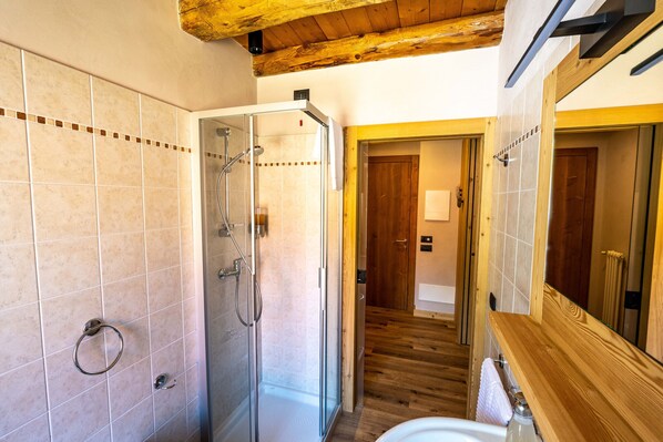 A bathroom with a glass shower enclosure, wooden floor, and a large mirror.