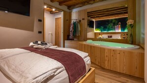 A modern bedroom with a large bed, a wooden ceiling, a built-in bathtub, and a TV mounted on the wall. - TEVERONE SUITES & WELLNESS - Camera Civetta (Lamosano)
