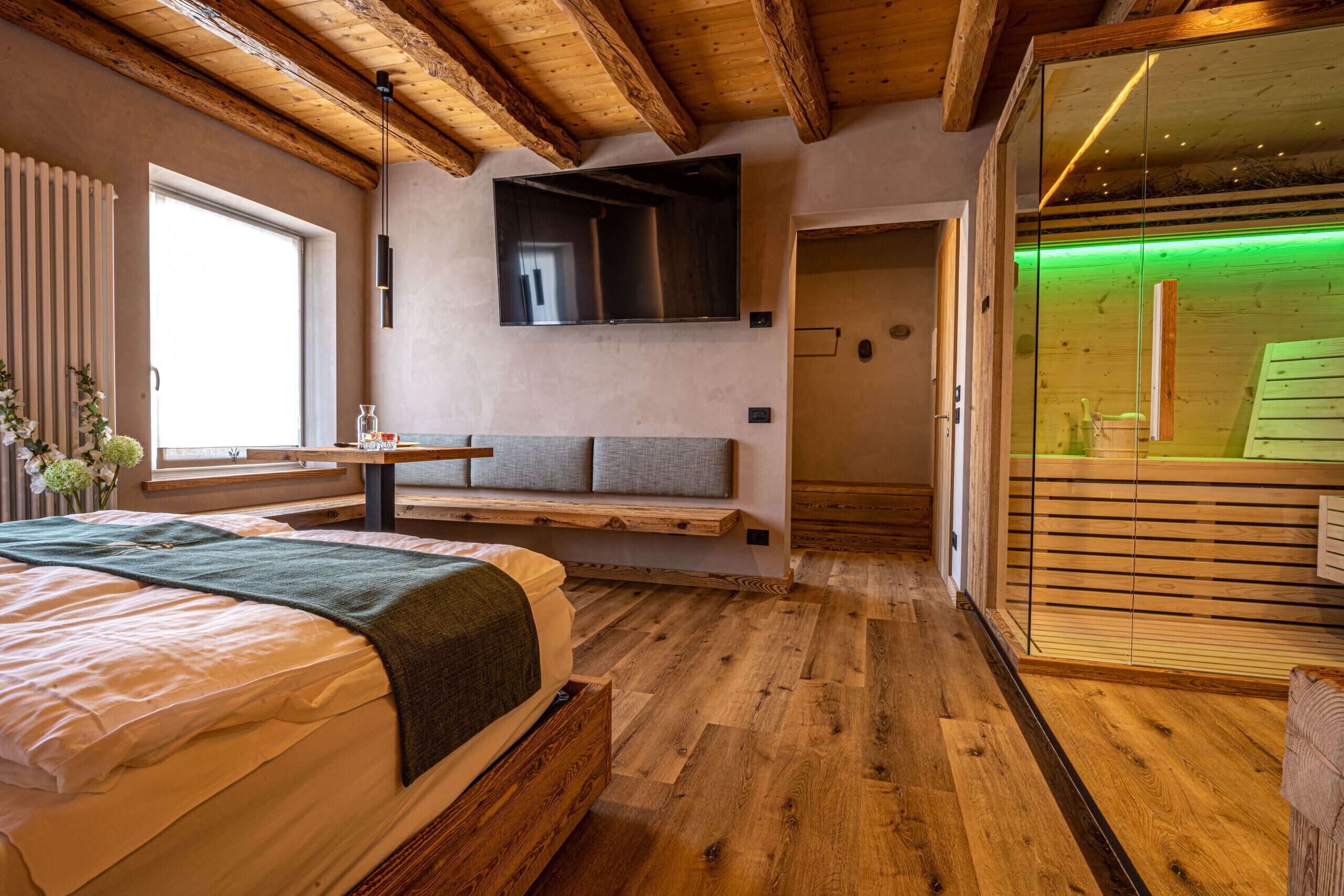 Ein Schlafzimmer mit einem Bett, einer Bank, einem Fernseher und einer Schiebetür zum Badezimmer.