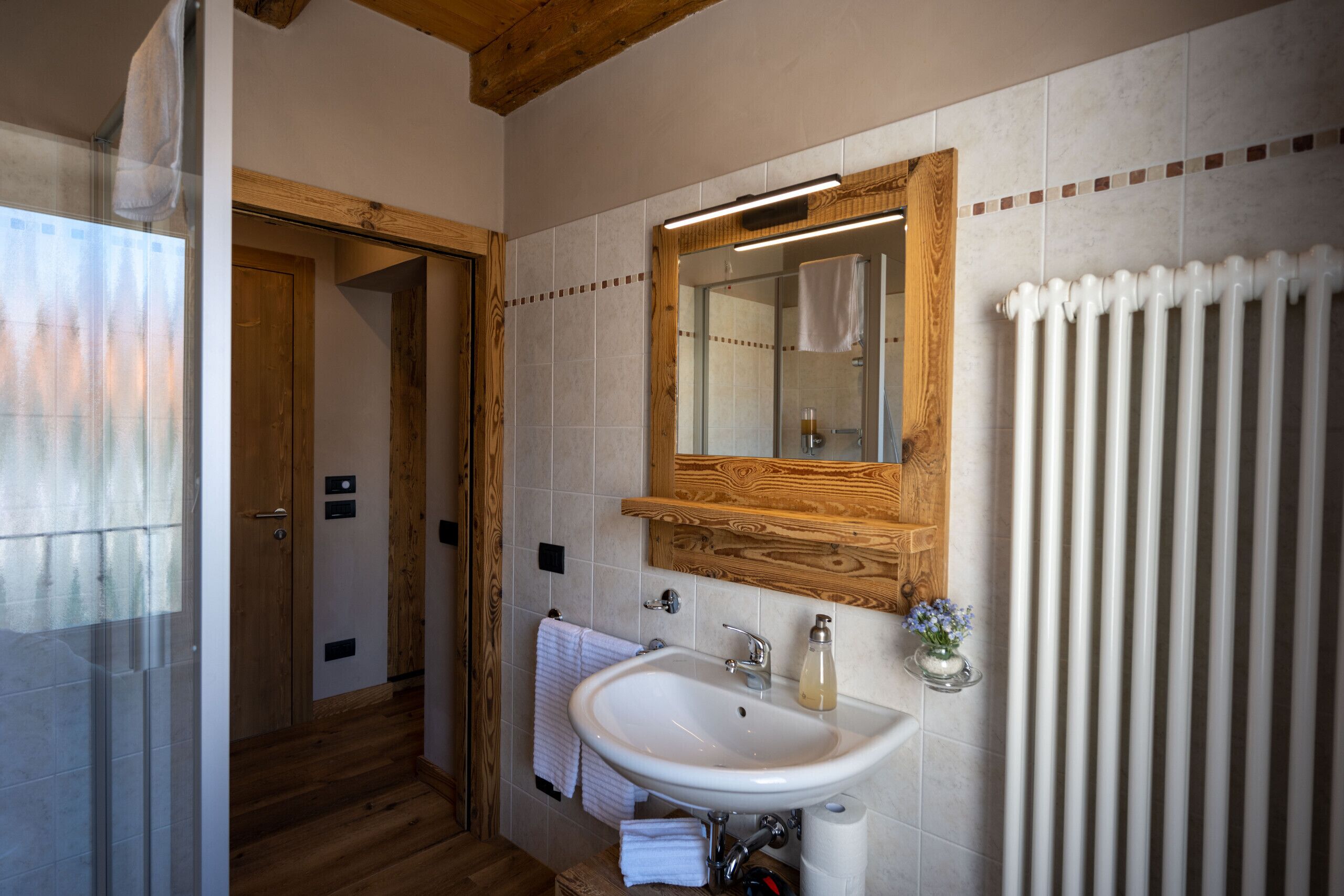 Un baño con puerta de madera, un lavabo blanco, un espejo y un radiador.