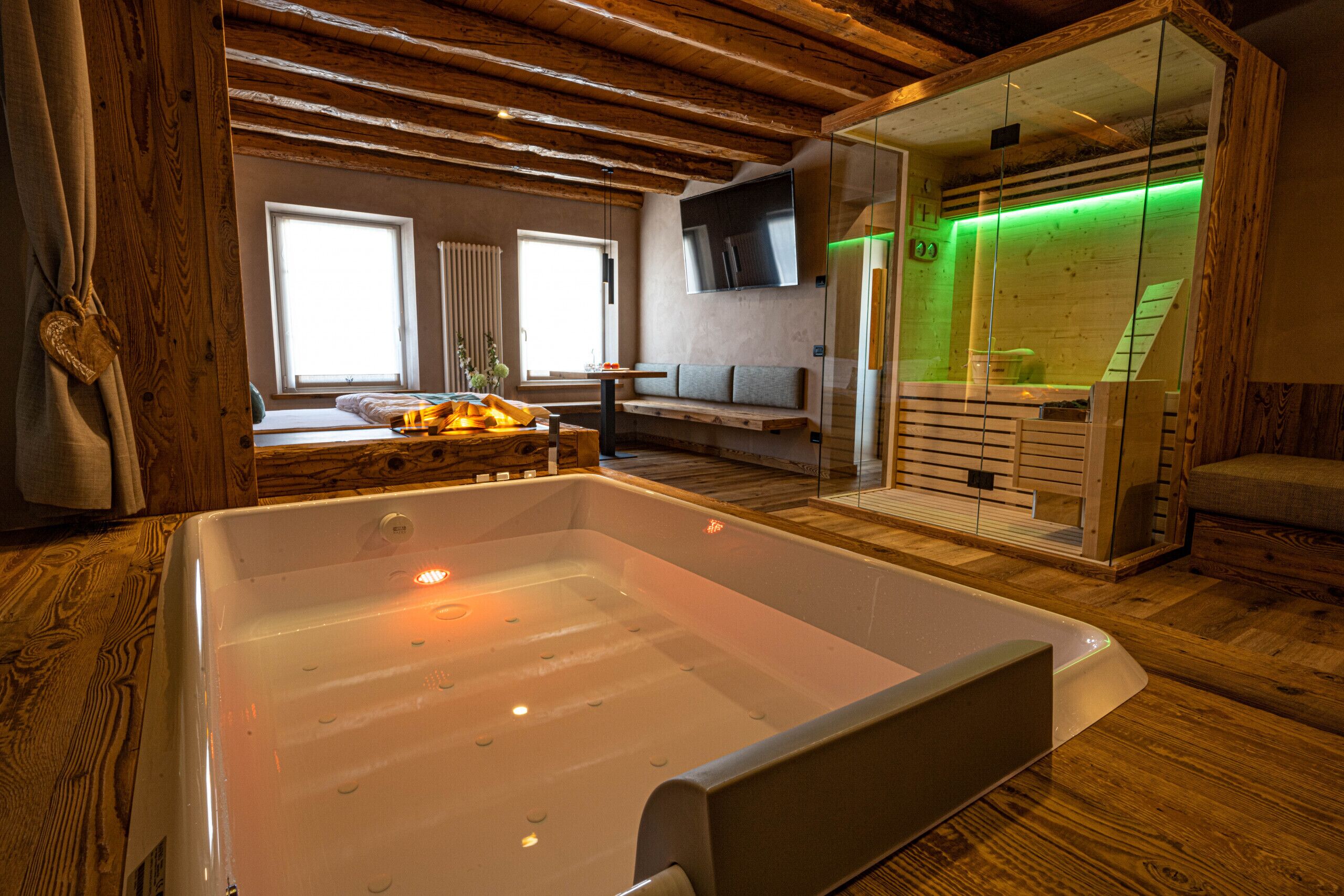 A modern spa room with a large bathtub, wooden floors, a sofa, and a television.