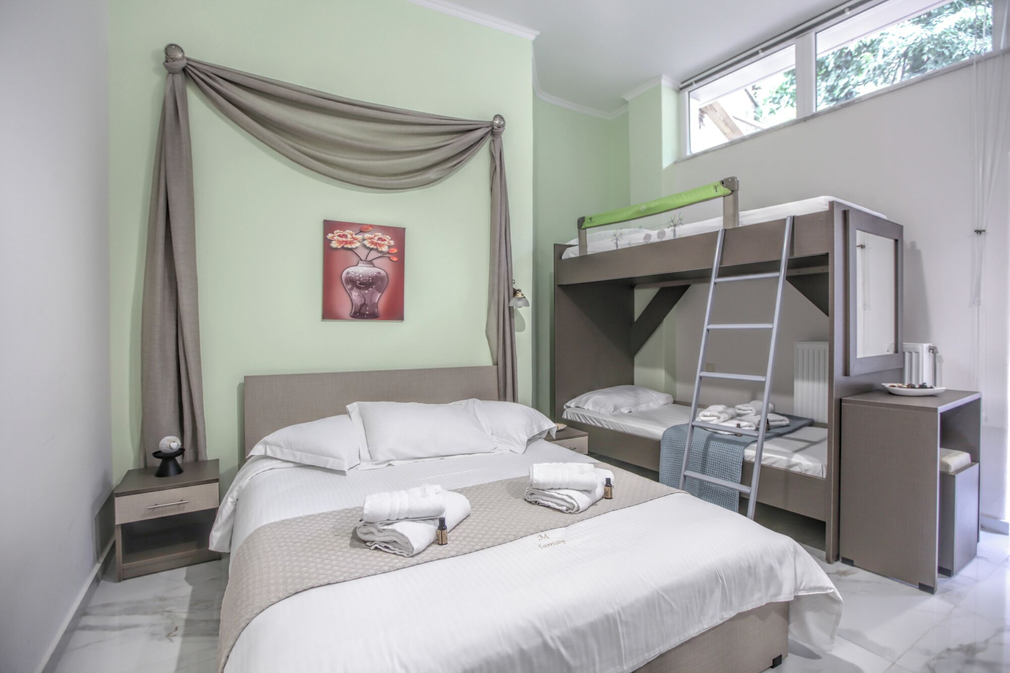 Quarto com uma cama grande, uma cama beliche, uma escada, mesa de cabeceira e uma janela.