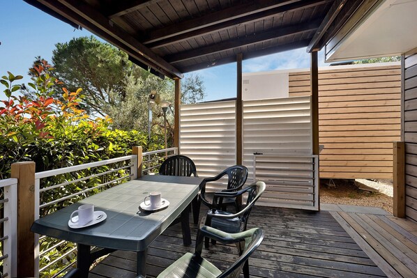 Une terrasse extérieure couverte, dotée d’une table et de chaises, entourée d’une terrasse en bois et d’une clôture blanche.