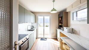 Una cocina moderna con un amplio ventanal, una lámpara colgante verde y vistas a la ciudad.