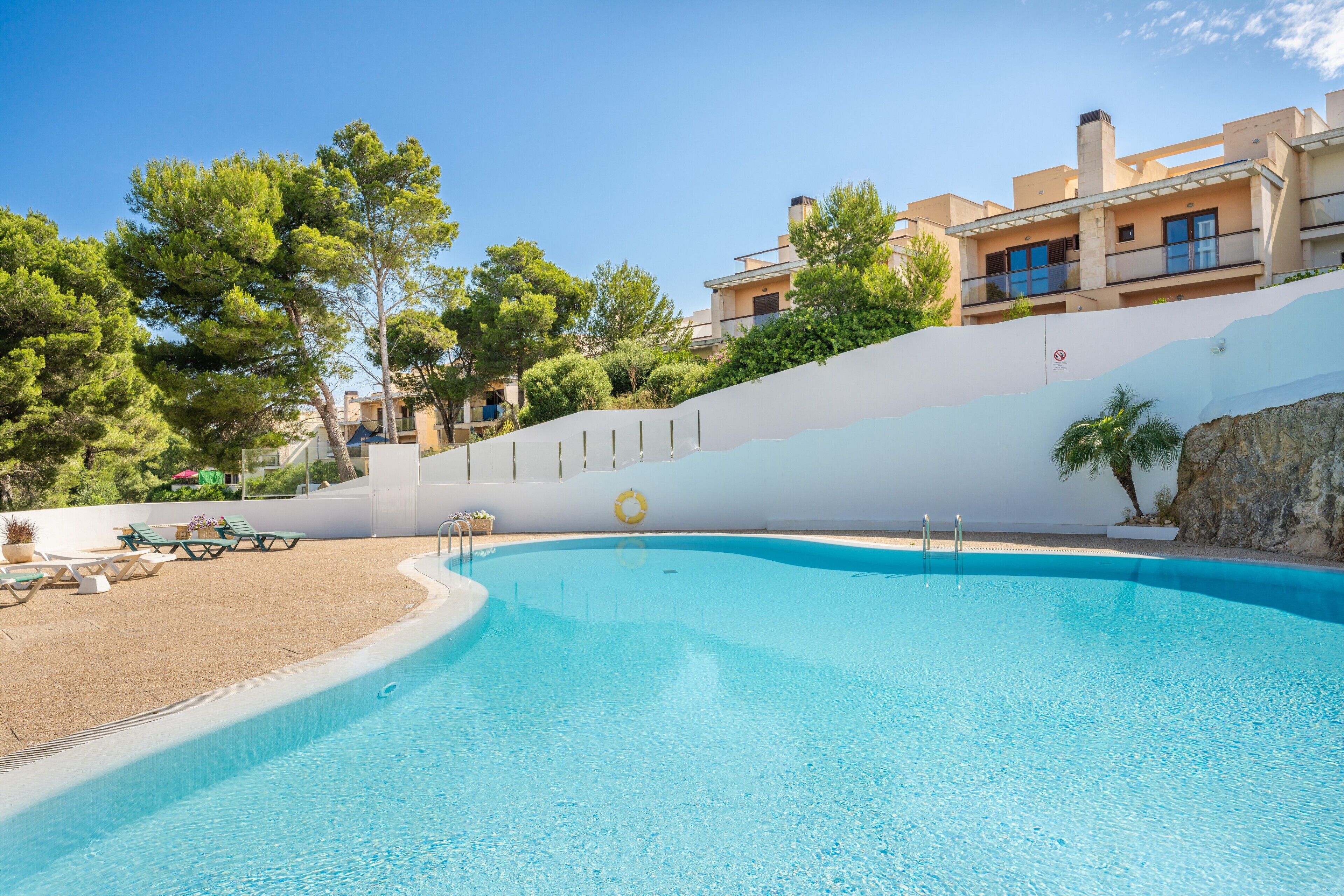 A swimming pool with lounge chairs and a lifebuoy, surrounded by buildings and trees.