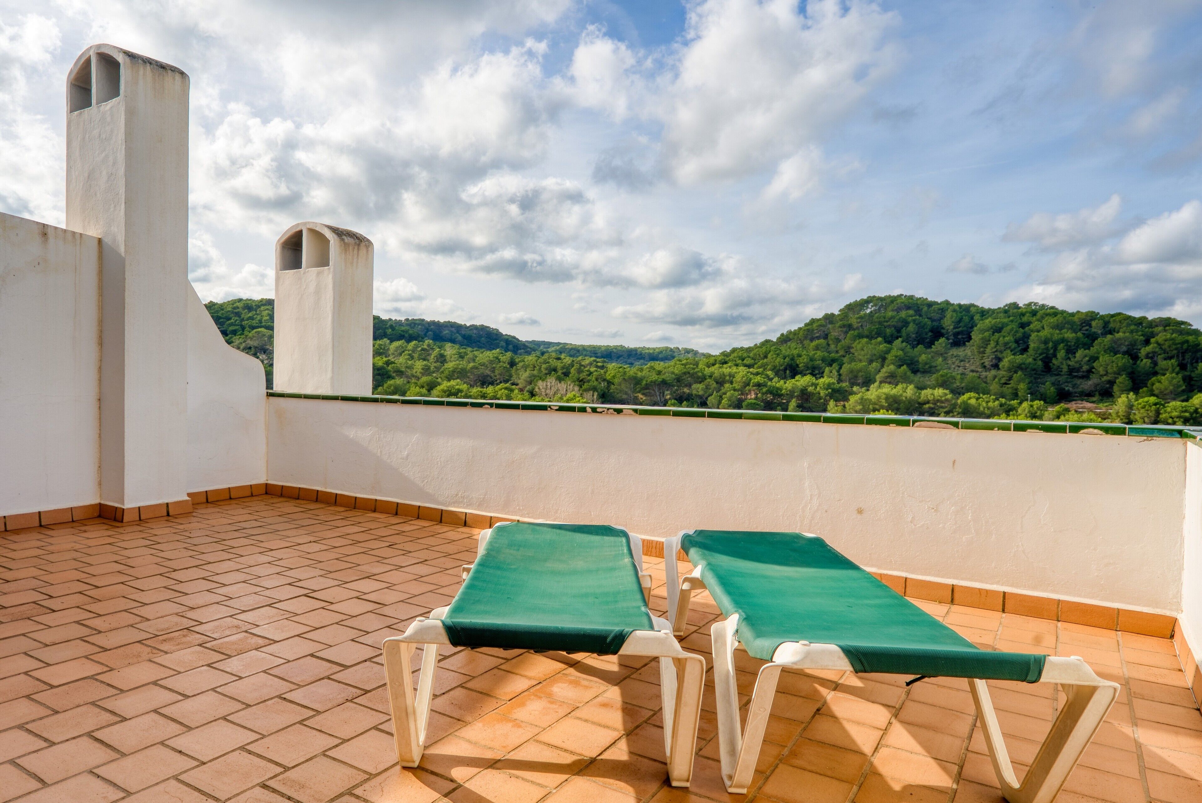 Una terraza en la azotea con dos tumbonas, suelo de baldosas y vistas a una ladera verde.