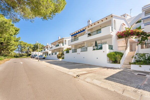 A residential street with white buildings, balconies, and a clear sky.