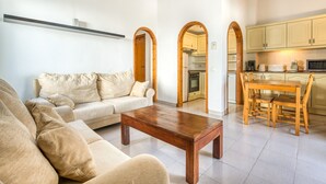A living room with a sofa, a wooden coffee table, and a kitchen area with cabinets and a dining table. - Apartment "Green Park B18" with Private Terraces, Shared Pool and Wi-Fi (Son Parc)