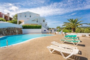 A swimming pool with lounge chairs, a modern building, and a palm tree.