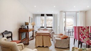A hotel room with a bed, two chairs, a table, a lamp, and a view of the outdoors.