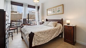 A bedroom with a bed, a desk, a chair, a wardrobe, and a window with curtains.