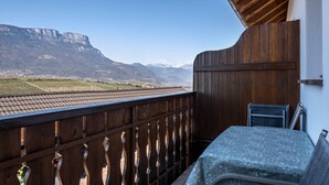 A balcony with a view of mountains, a wooden railing, and a table with a tablecloth. - Farmhouse "Valtlhof - Apt 2" with Shared Pool, Shared Garden & Wi-Fi (Cornaiano)